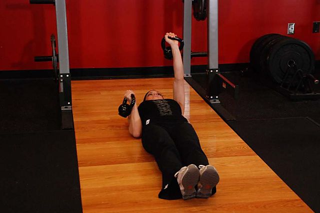 Фото упражнения Поочередный жим гирь лежа на полу